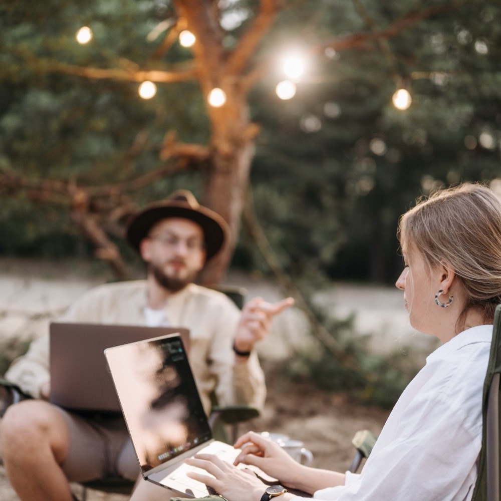 Two colleagues working on laptops outdoors under string lights